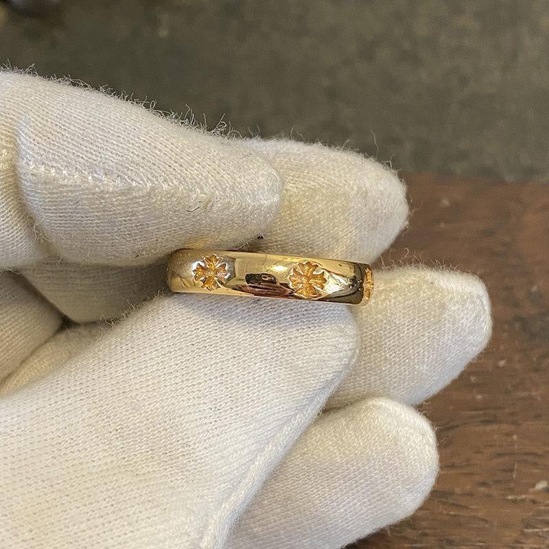Gold-colored ring held in glove with engraved floral details and dark inlay strip.
