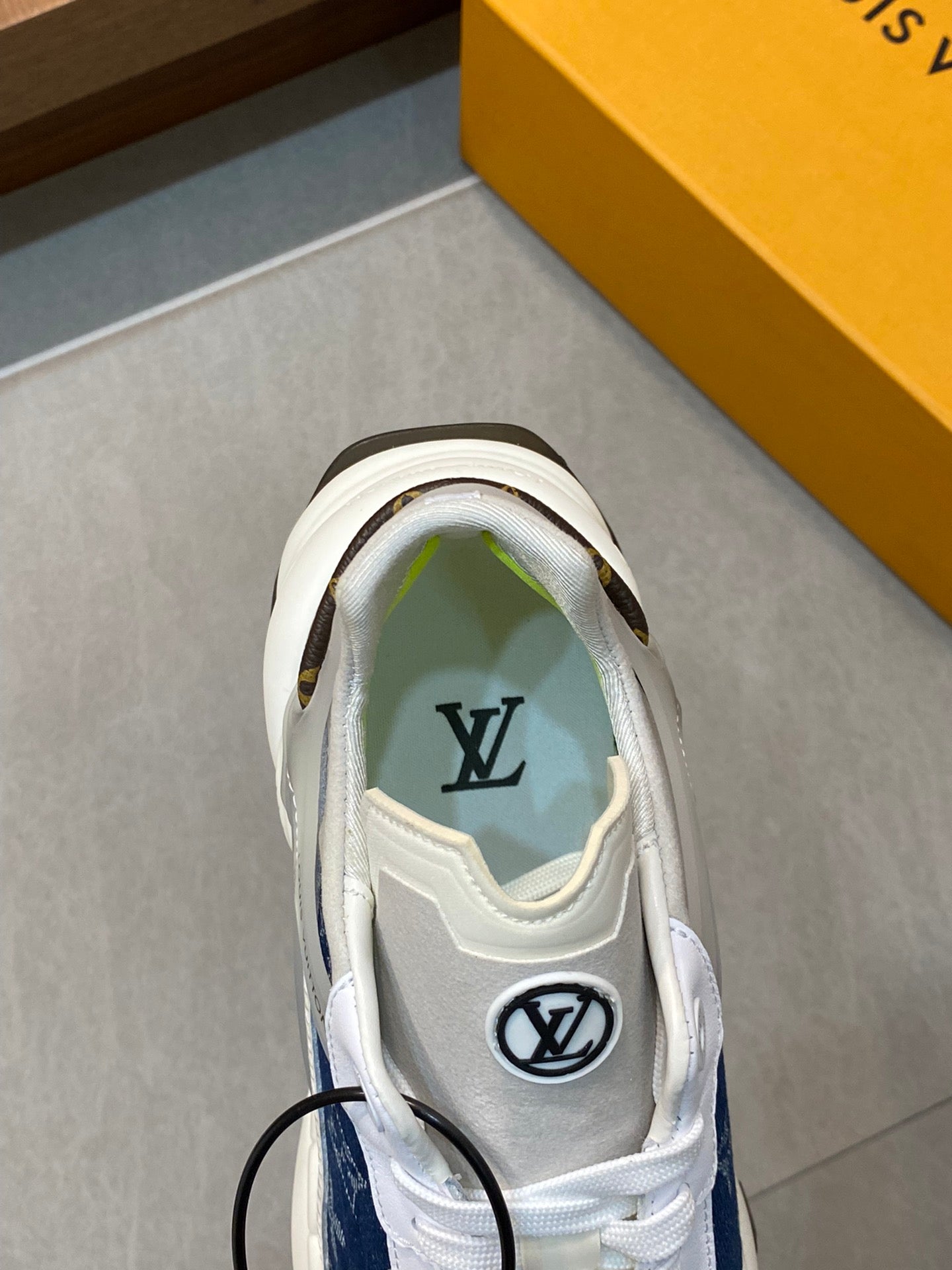 White unisex sneaker with blue monogram accent at collar, lace-up