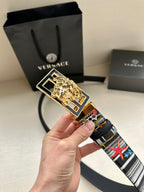 Versace belt held close-up with gold lion buckle and multicolor graphic strap
