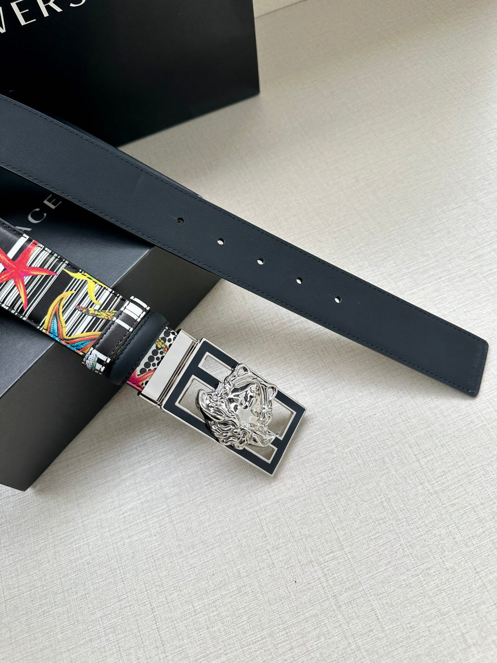 Versace belt laid flat with multicolor graphic strap and silver lion buckle