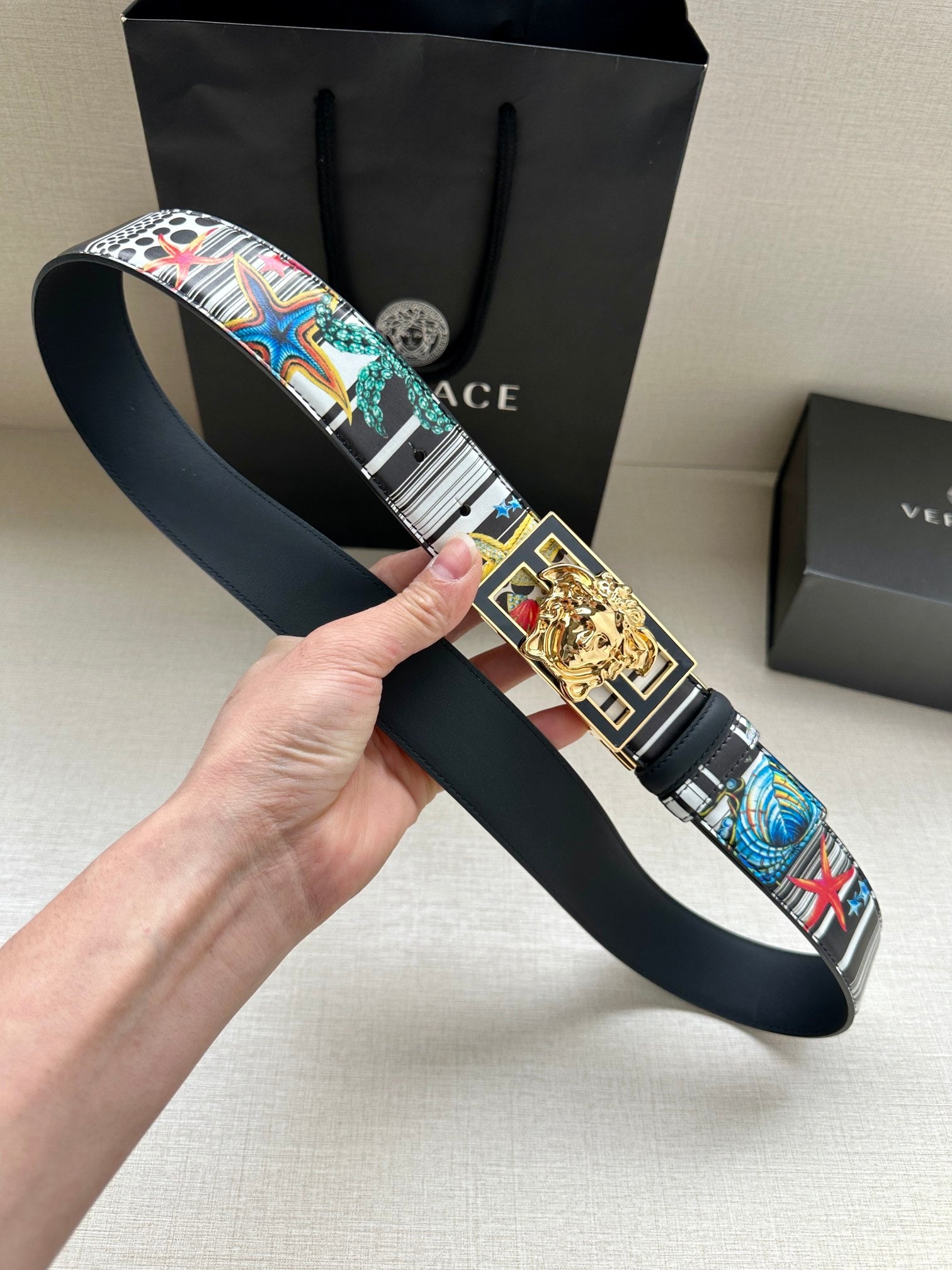 Versace belt held in hand with multicolor strap and gold lion buckle