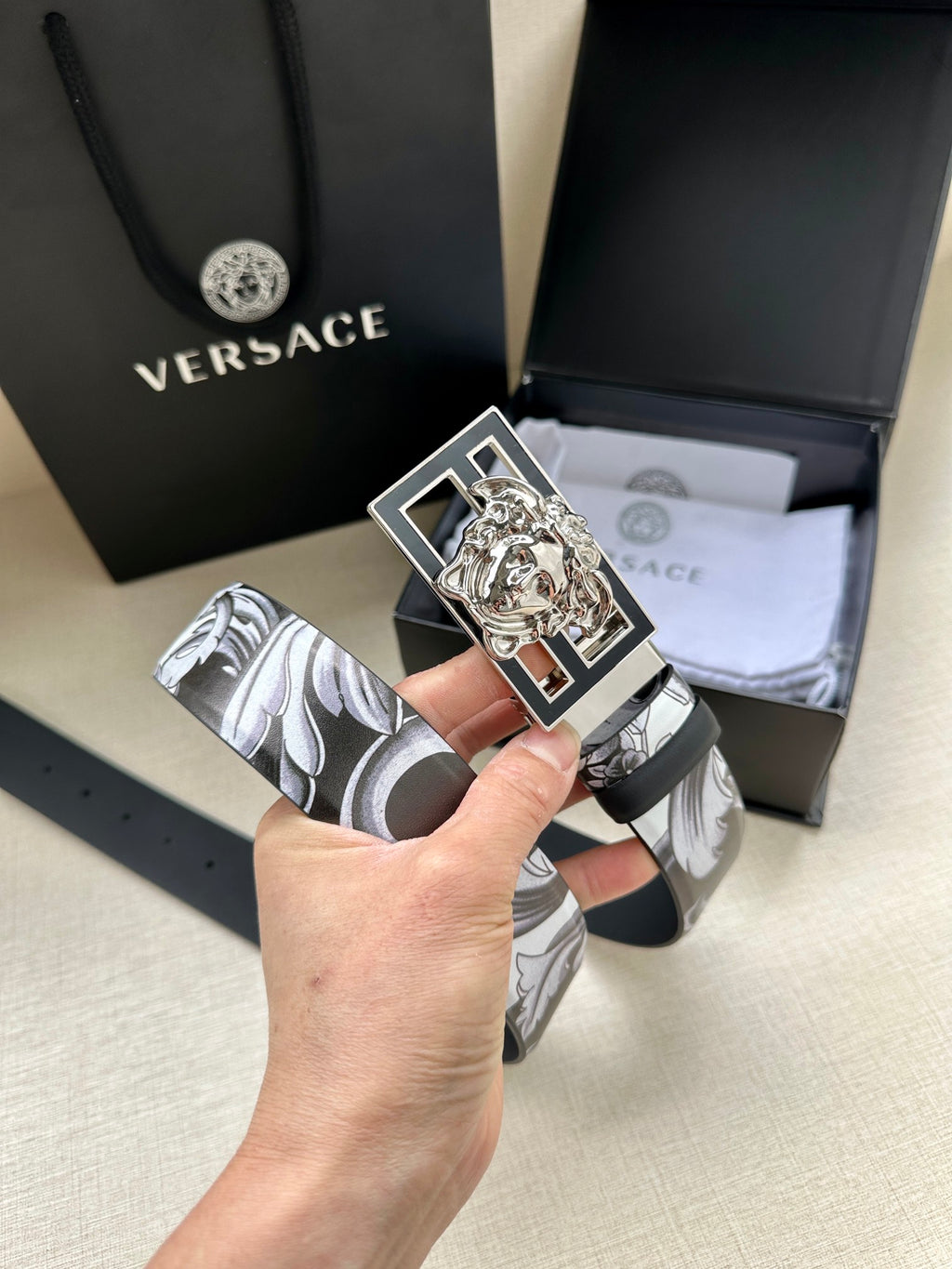 Belt with gray floral print strap and silver buckle with gold Medusa head.