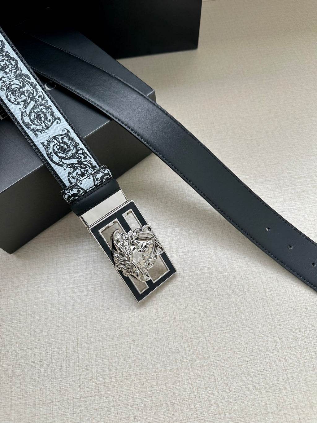 Designer belt detail: dark strap with baroque trim and silver-toned square buckle