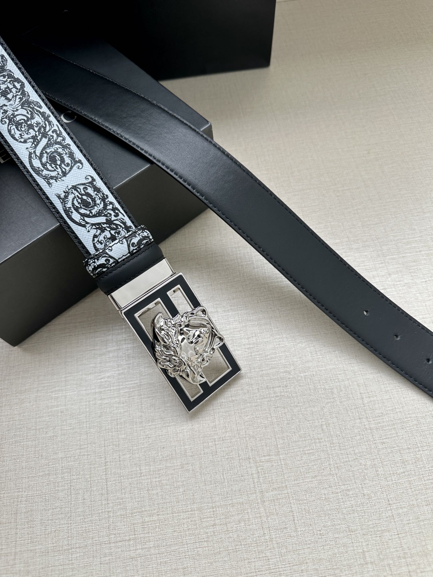 Designer belt detail: dark strap with baroque trim and silver-toned square buckle