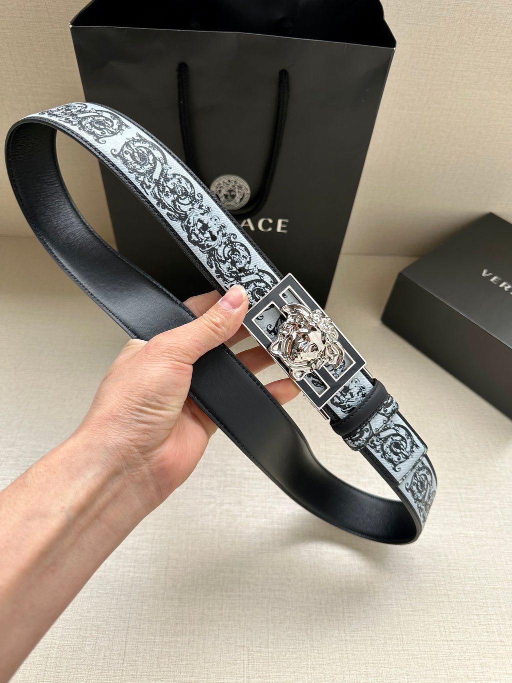 Designer belt on hand: patterned strap with large silver square buckle and Medusa motif