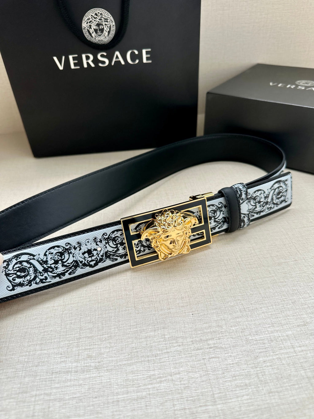 Designer belt lying flat with patterned strap and gold-tone Medusa buckle with black inset
