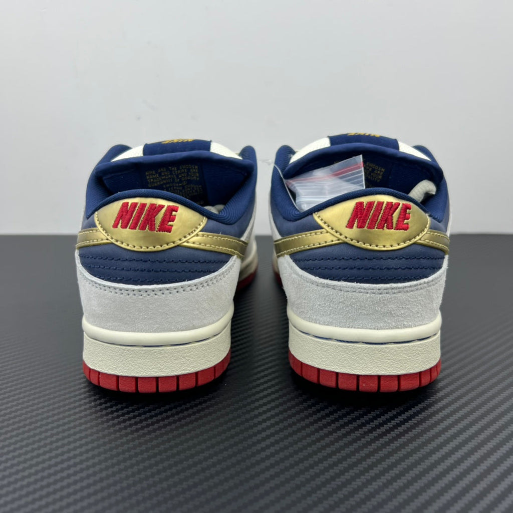 Back view of low-top sneakers with white uppers, navy collars, gold trim, red soles.