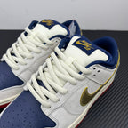 Angled view of low-top sneakers with white uppers, navy SBD patch, gold swoosh.