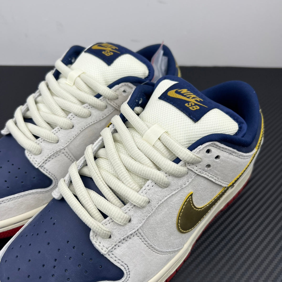Angled view of low-top sneakers with white uppers, navy SBD patch, gold swoosh.
