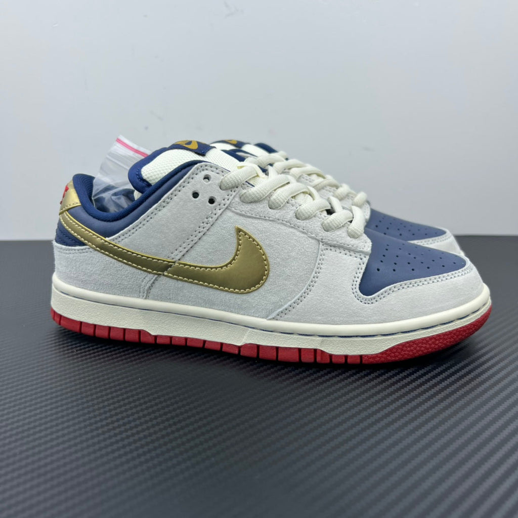 Low-top sneaker in light gray/white with gold swoosh, navy panels, red outsole.