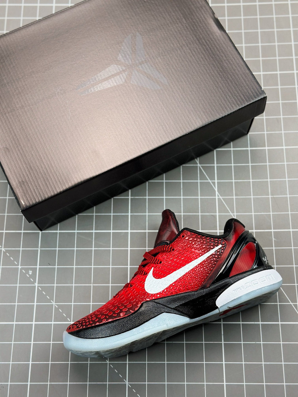 Red and black basketball shoe on box, side view with white swoosh and light sole