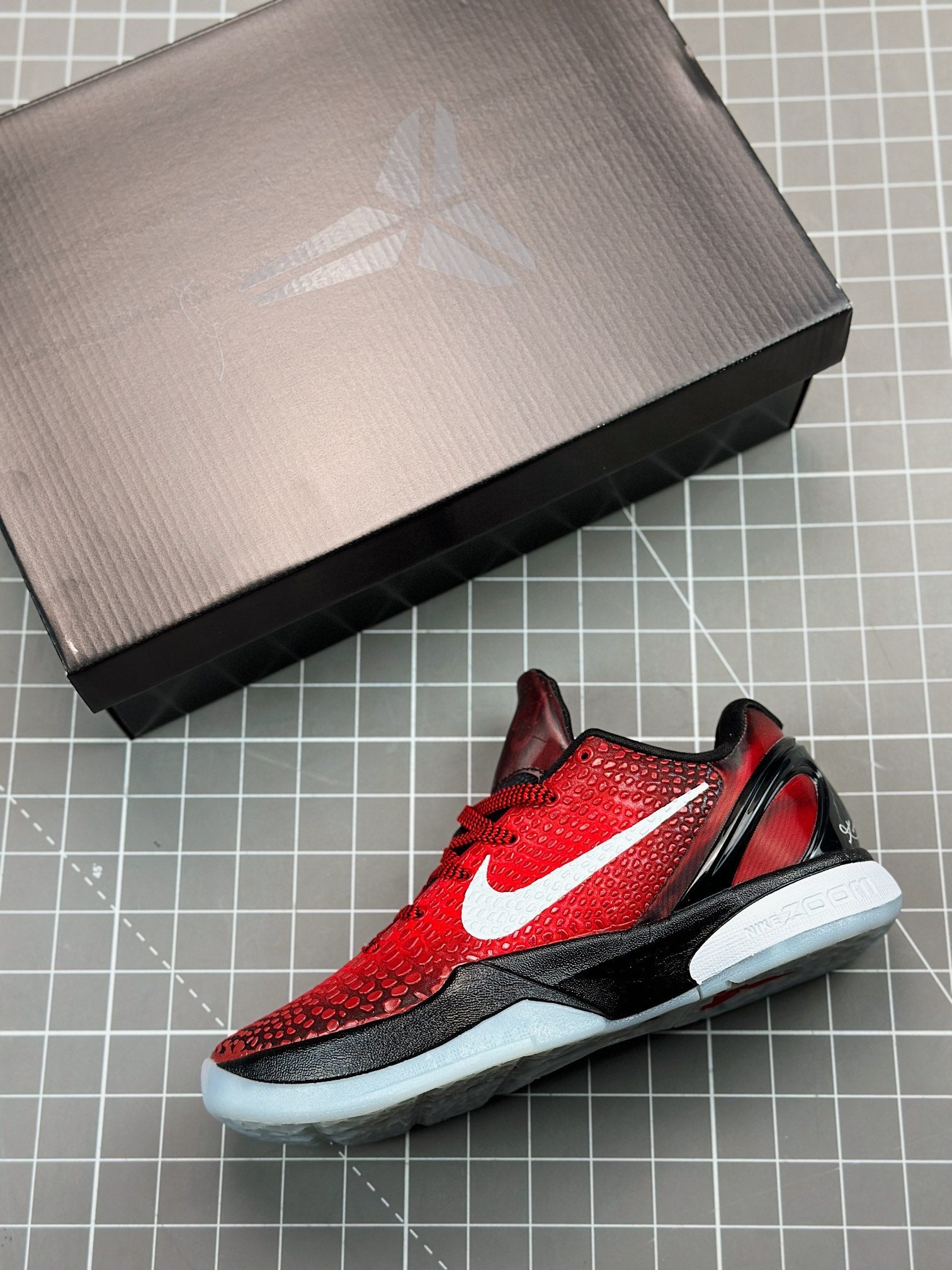 Red and black basketball shoe on box, side view with white swoosh and light sole
