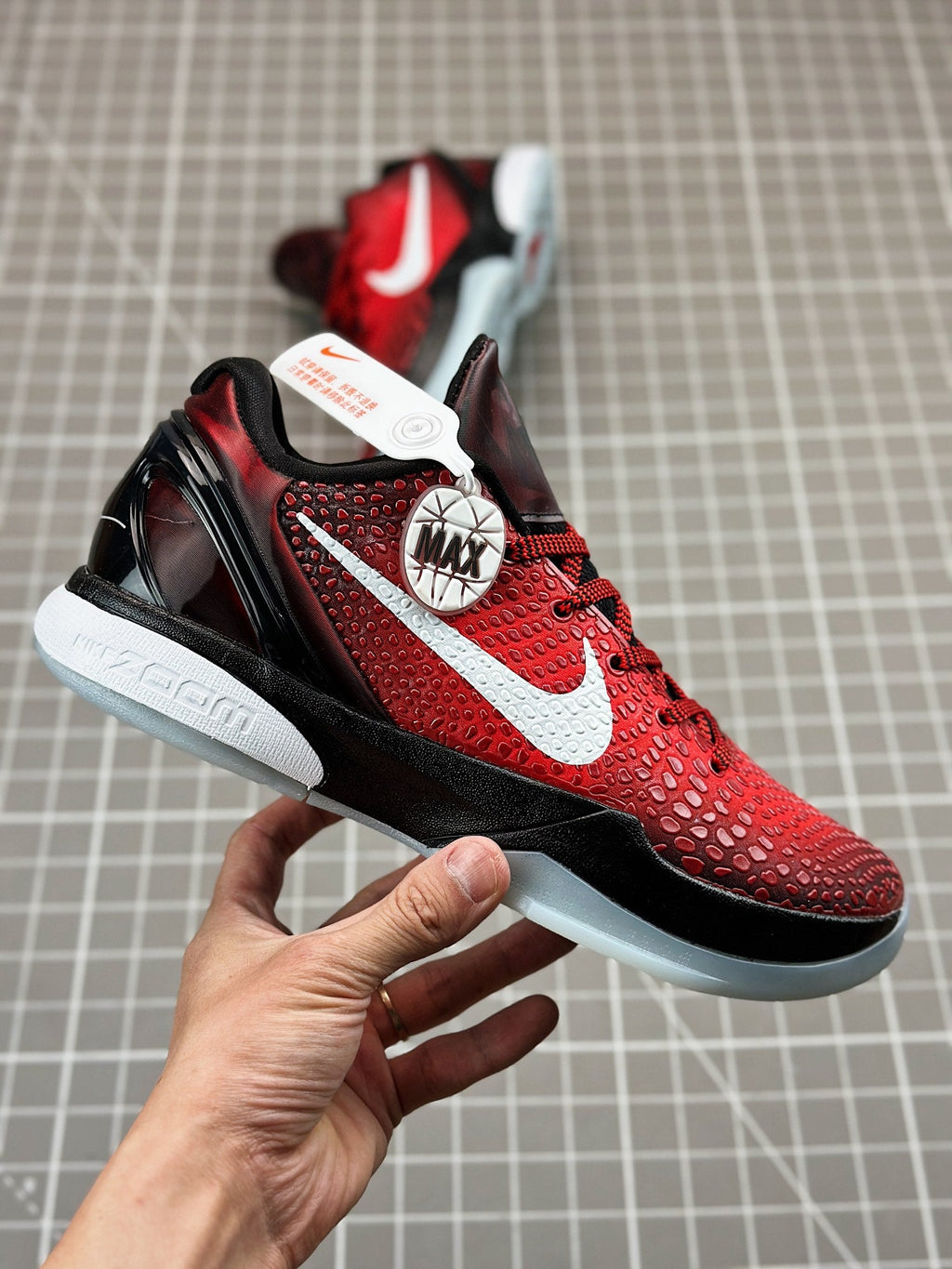 Red basketball shoe side view held in hand, white swoosh and black detail midsole