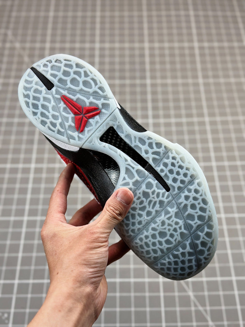 Shoe outsole with white traction pattern, black and red upper visible at heel