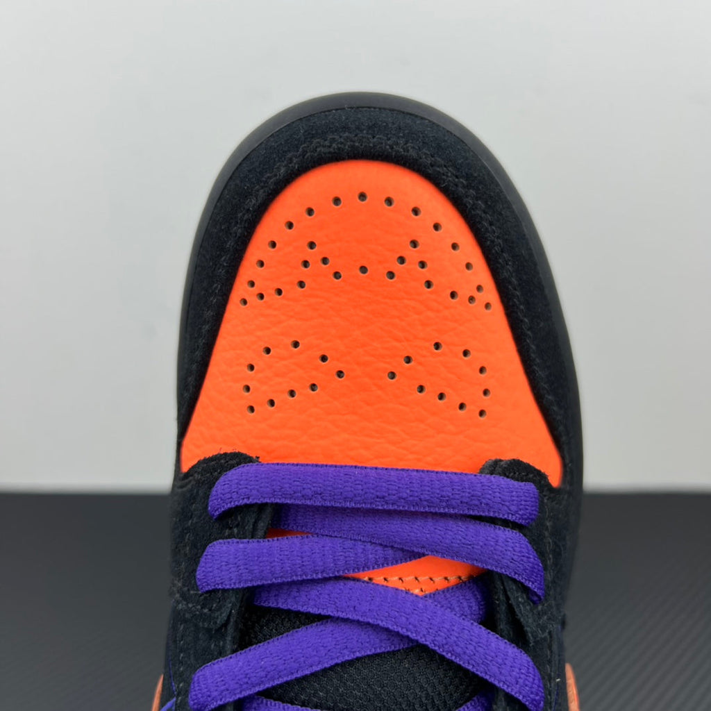 Front toe view of black sneaker with orange panel and purple laces.