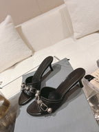 Black leather heeled mule sandals with metal buckle cross-strap detail