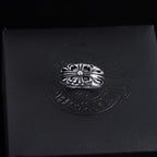 Silver-tone ornate chrome ring with central round gemstone and braided-looking band.