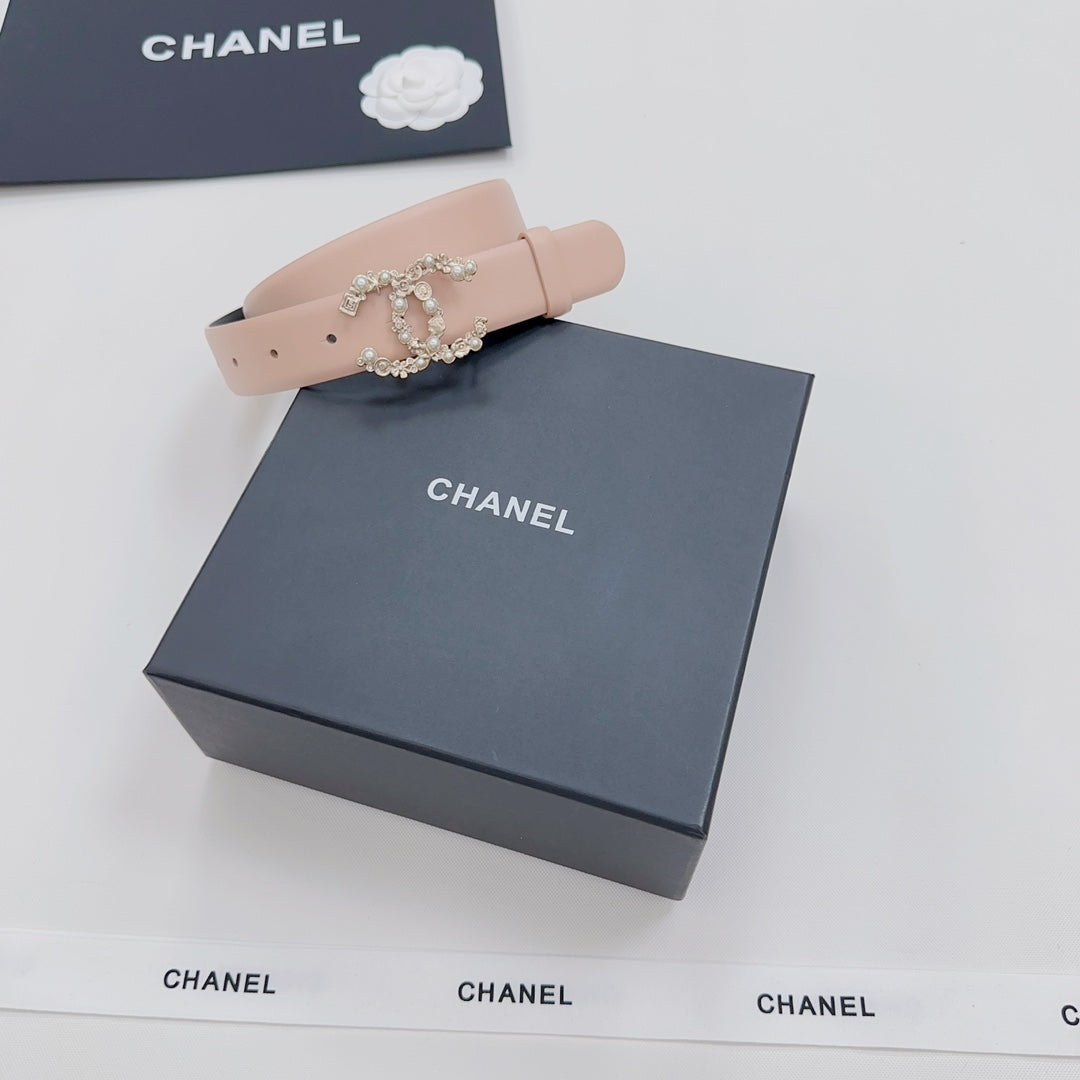 Light pink leather belt with ornate rhinestone buckle, placed on a dark box