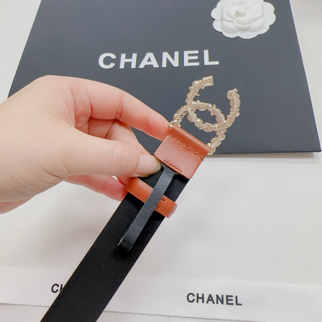 Orange-and-black belt end with silver-tone CC-style buckle, hand holding.