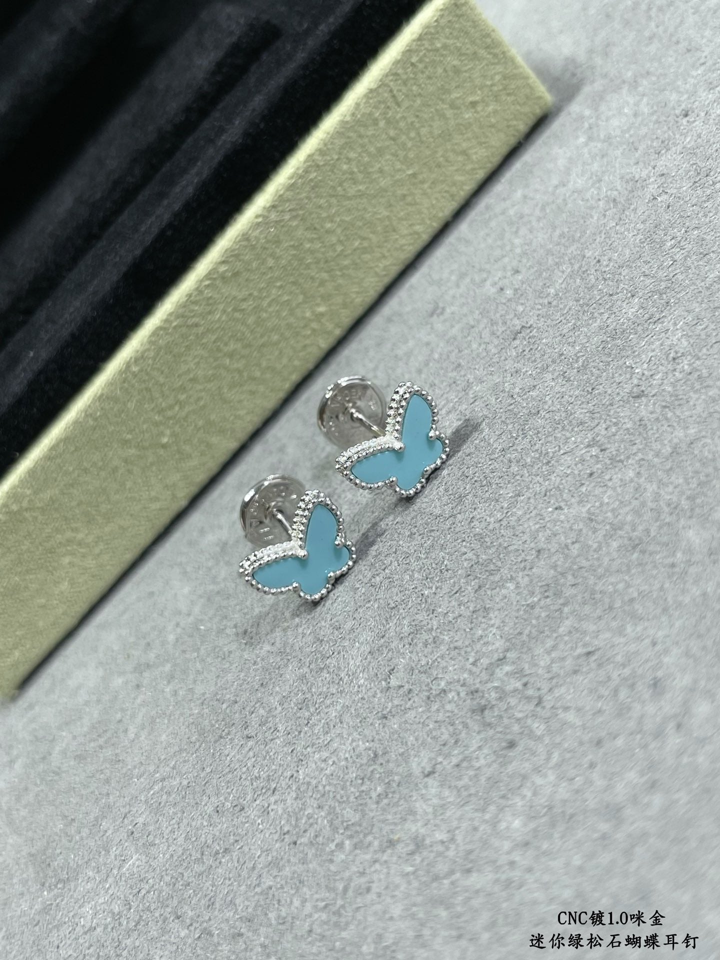 Butterfly stud earrings pair on light fabric, blue enamel wings with silver-tone setting.