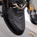 Close-up of black embossed leather loafer with silver buckle and medallion.