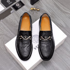 Black embossed leather loafers with silver buckle and emblem detail.