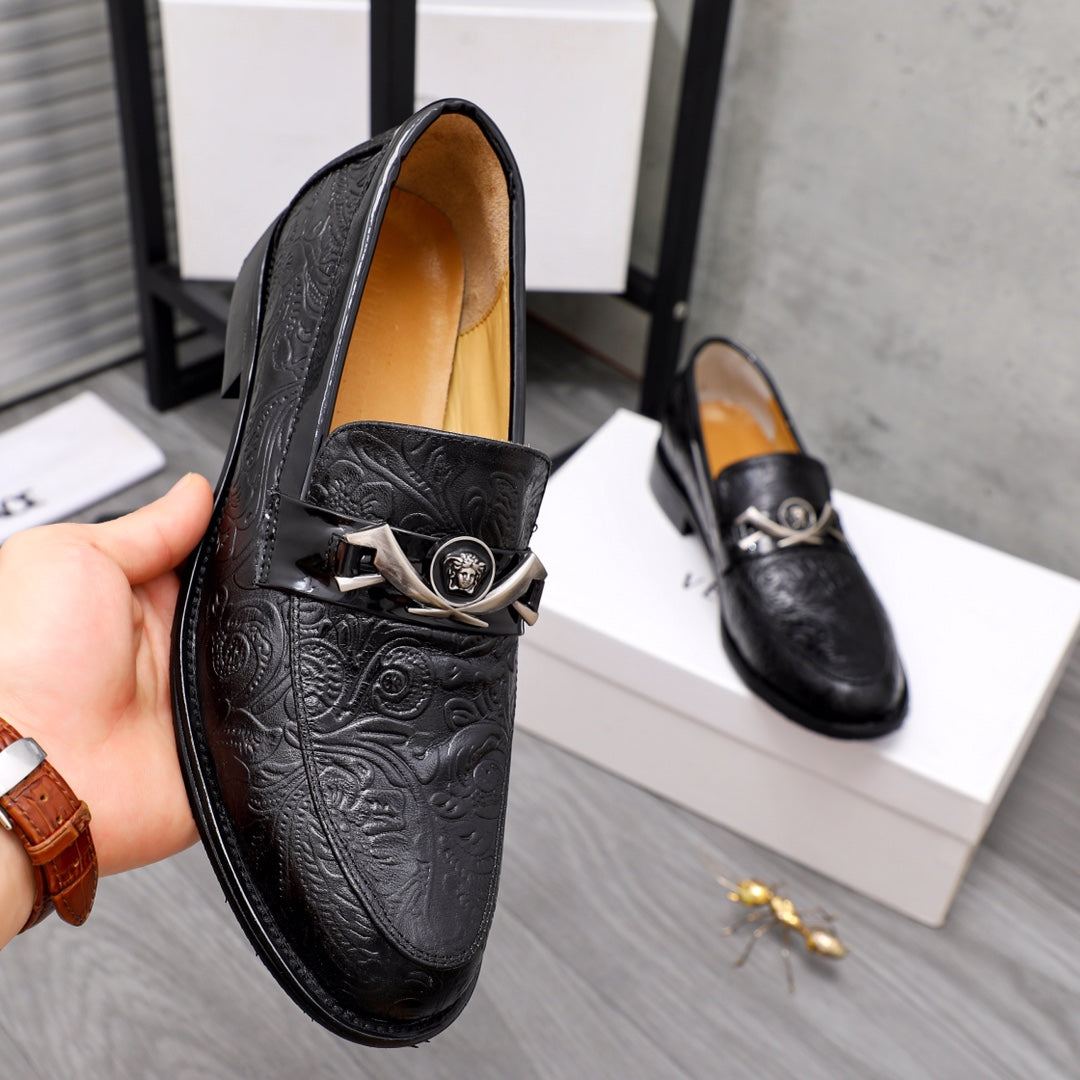 Black embossed leather loafers front close-up with silver buckle and emblem.