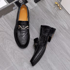 Pair of black embossed leather loafers with silver buckles and tan lining.