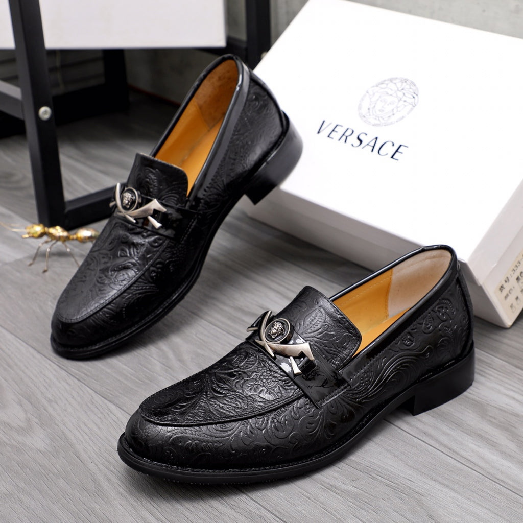 Black embossed leather loafers angled view, slip-on with silver buckle strap.