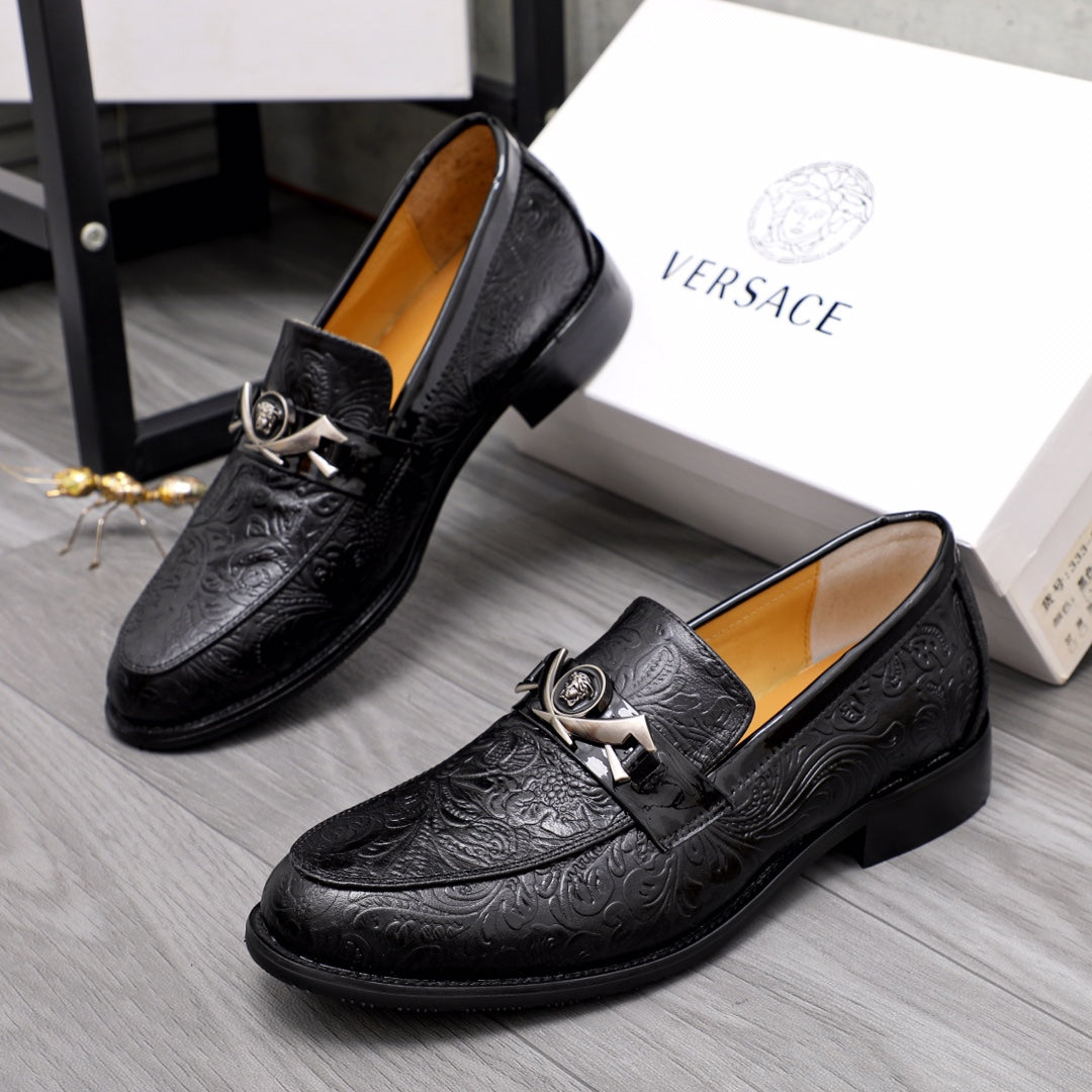 Black embossed leather loafers angled view, slip-on with silver buckle strap.