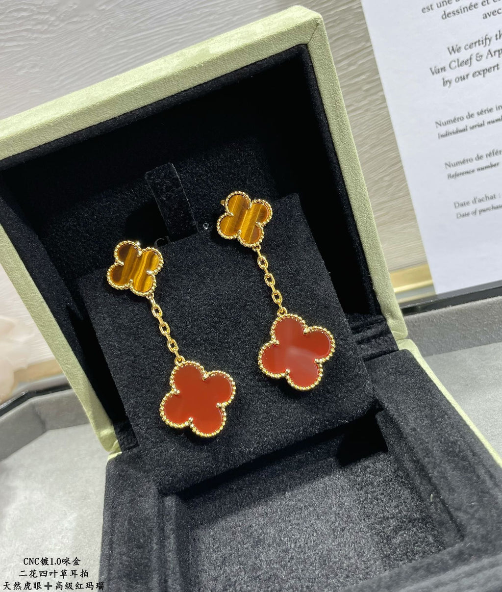 Gold-tone clover drop earrings with red enamel, displayed in jewelry box