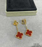 Gold-tone clover drop earrings with red enamel and chain dangles, on display