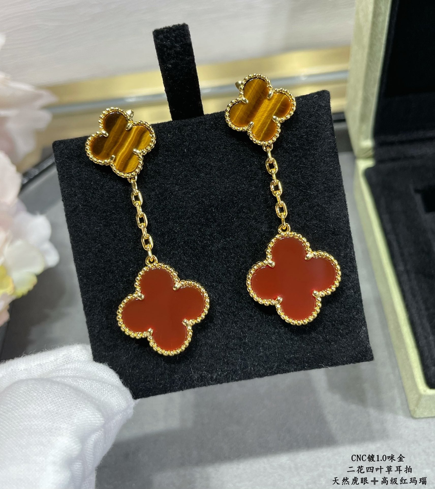 Gold-tone clover drop earrings with red enamel, front view on black insert