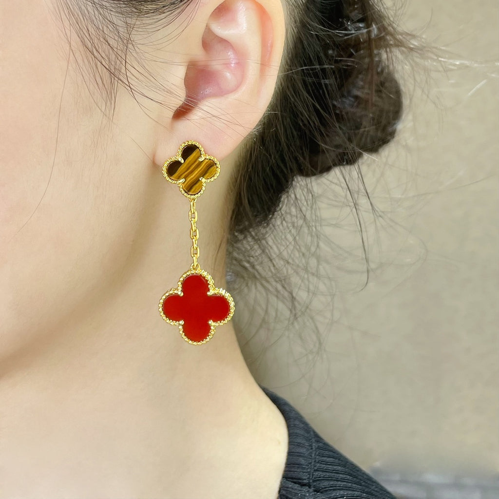 Gold-tone clover stud earrings with red enamel drop, shown on ear