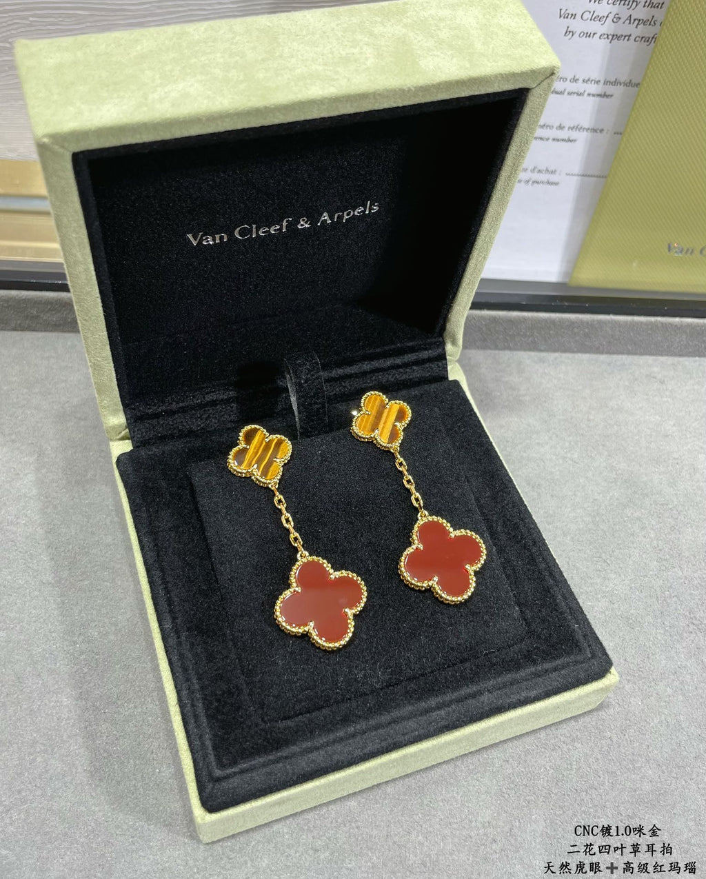 Gold-tone clover drop earrings with red enamel, in open black jewelry box