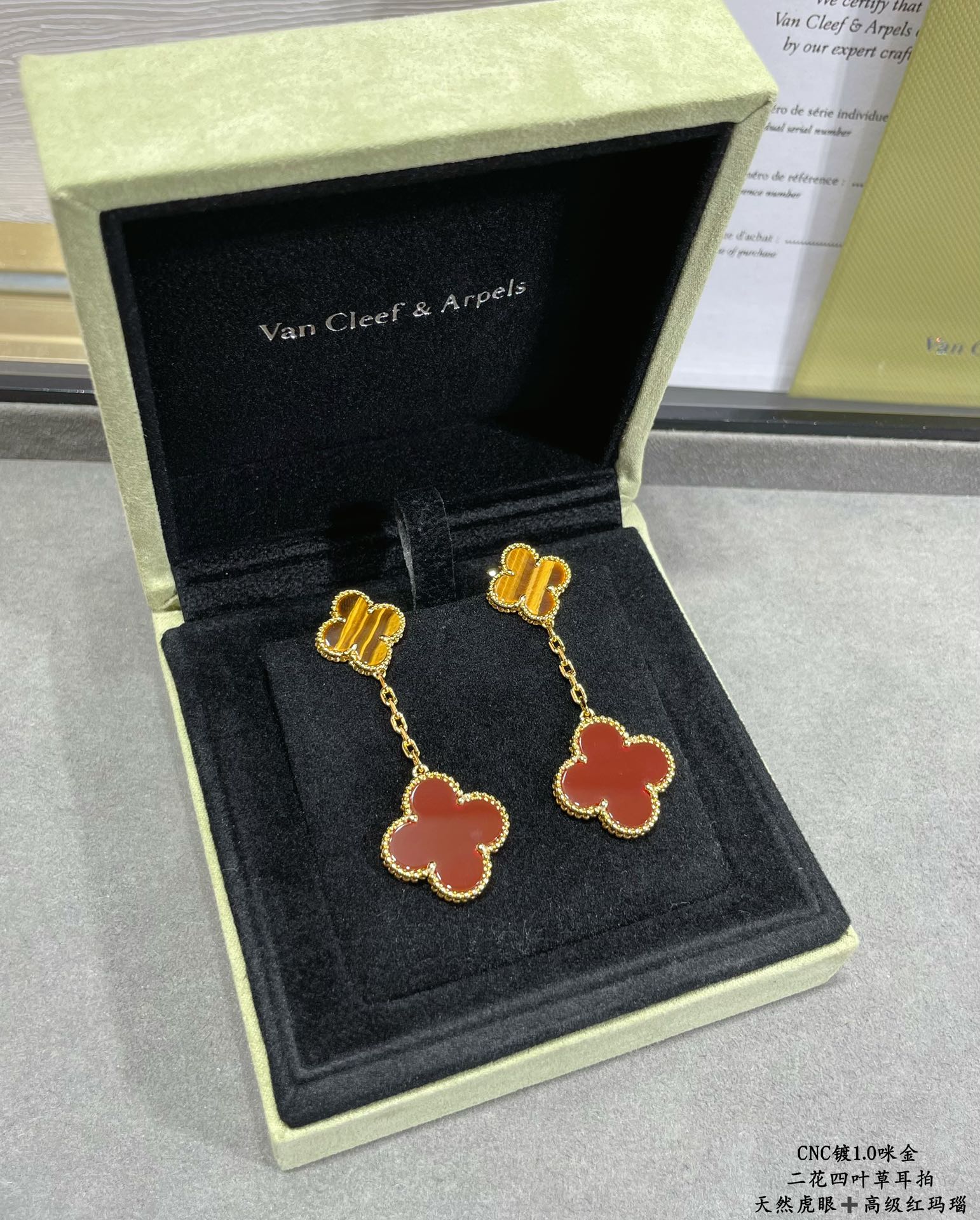 Gold-tone clover drop earrings with red enamel, in open black jewelry box