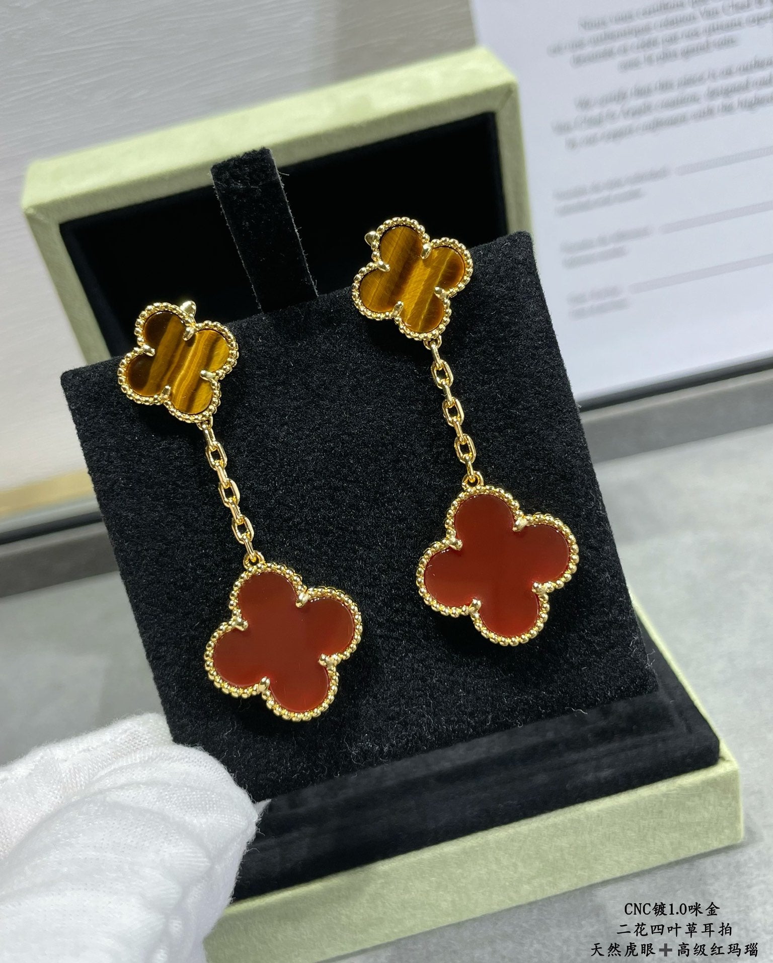 Gold-tone clover drop earrings with red enamel and gold chain, in box on tray