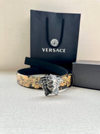 Leather belt with gold baroque pattern and silver Medusa buckle on dark navy strap.