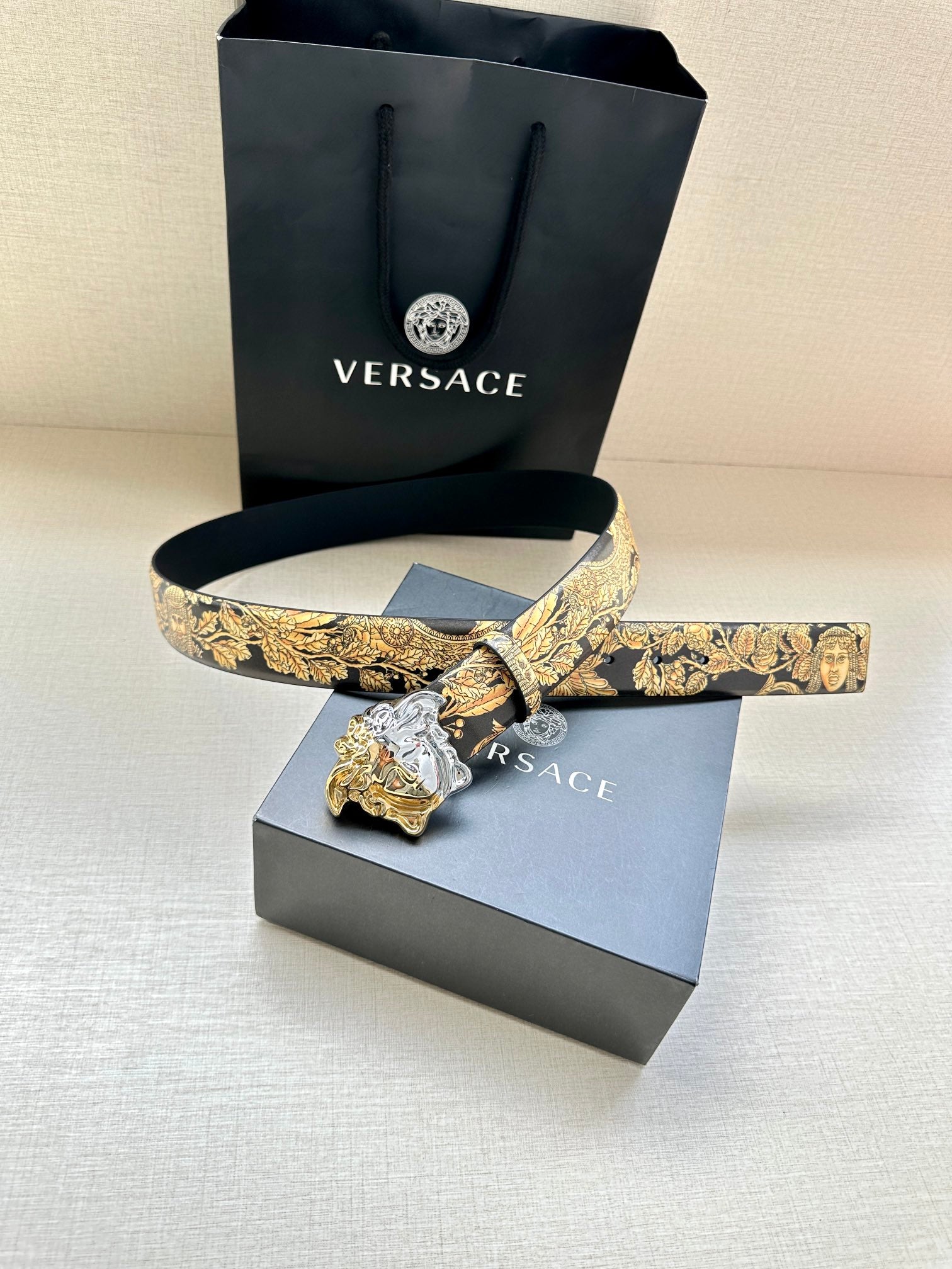 Leather belt with gold baroque print and silver Medusa buckle on dark navy leather strap.