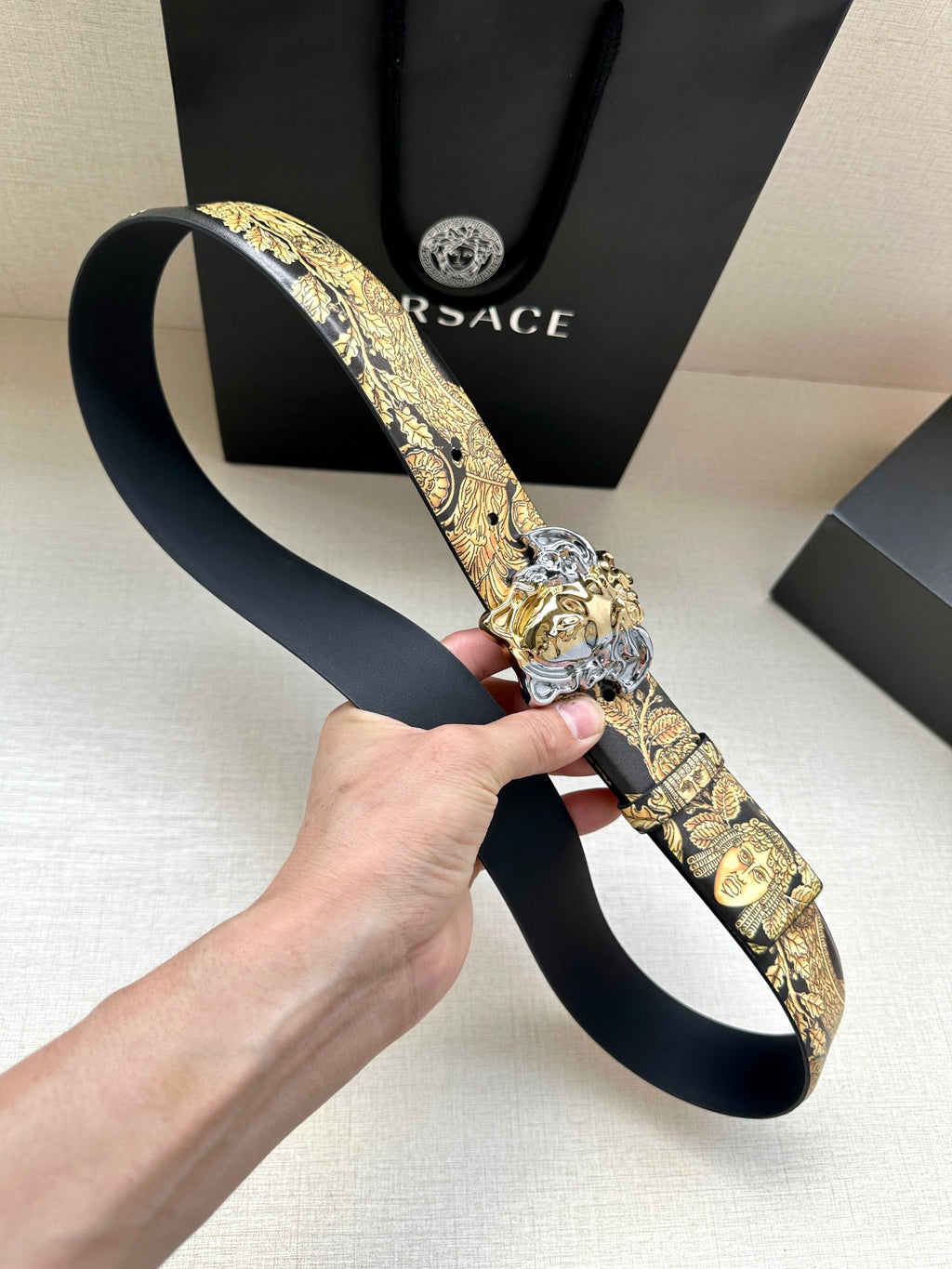 Leather belt laid out: dark navy leather with gold baroque print and silver Medusa buckle.