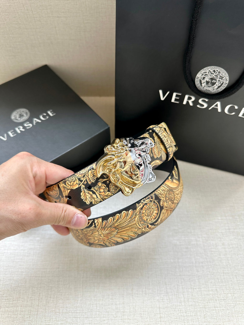 Leather belt buckle view: silver Medusa on gold printed leather strap, dark navy belt.