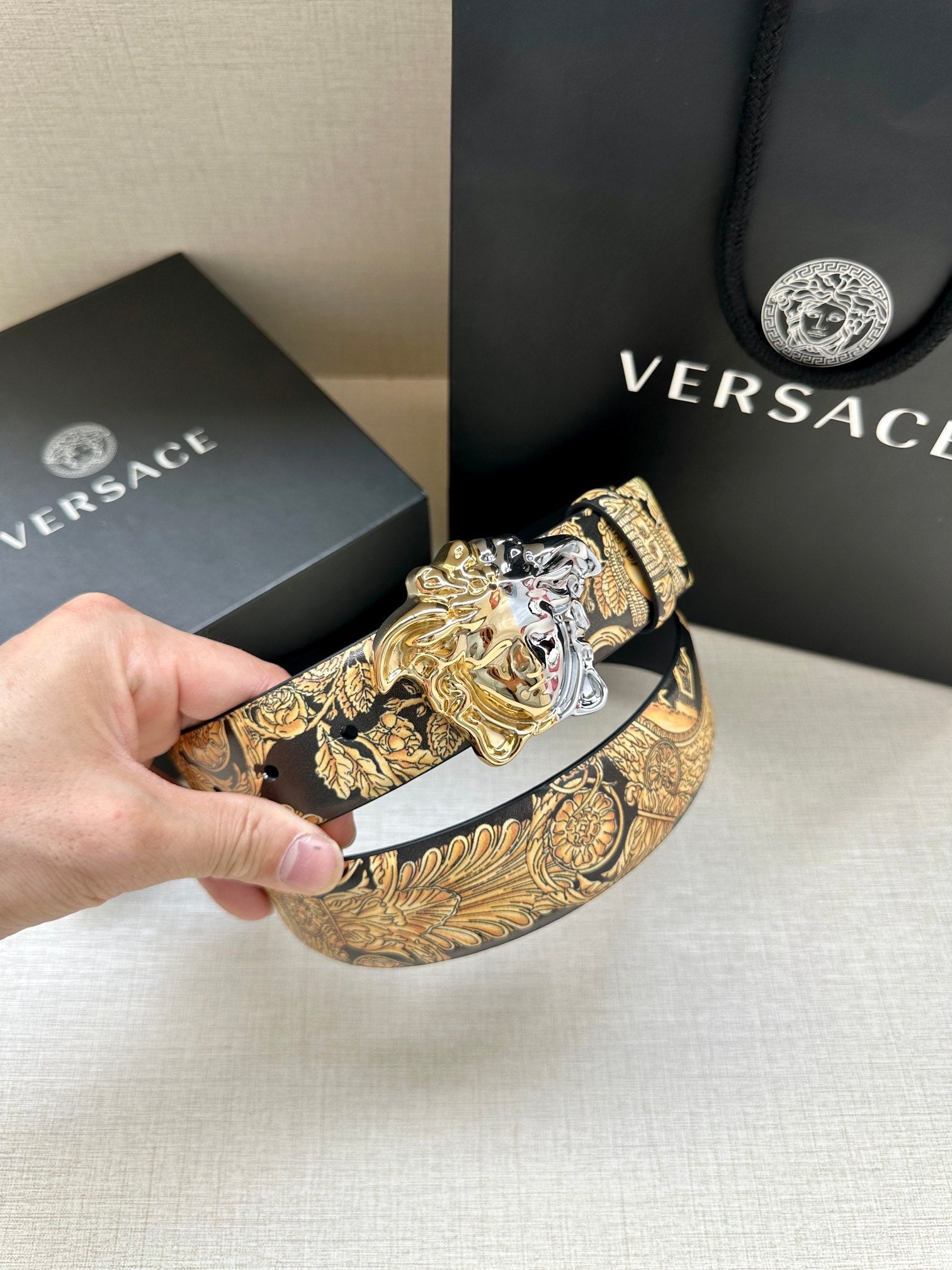 Leather belt buckle view: silver Medusa on gold printed leather strap, dark navy belt.