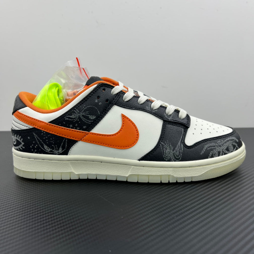 Low-top sneakers with white upper, black toe and side, orange Swoosh, white laces.