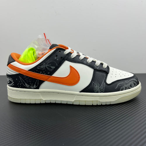 Low-top sneakers with white upper, black toe and side, orange Swoosh, white laces.