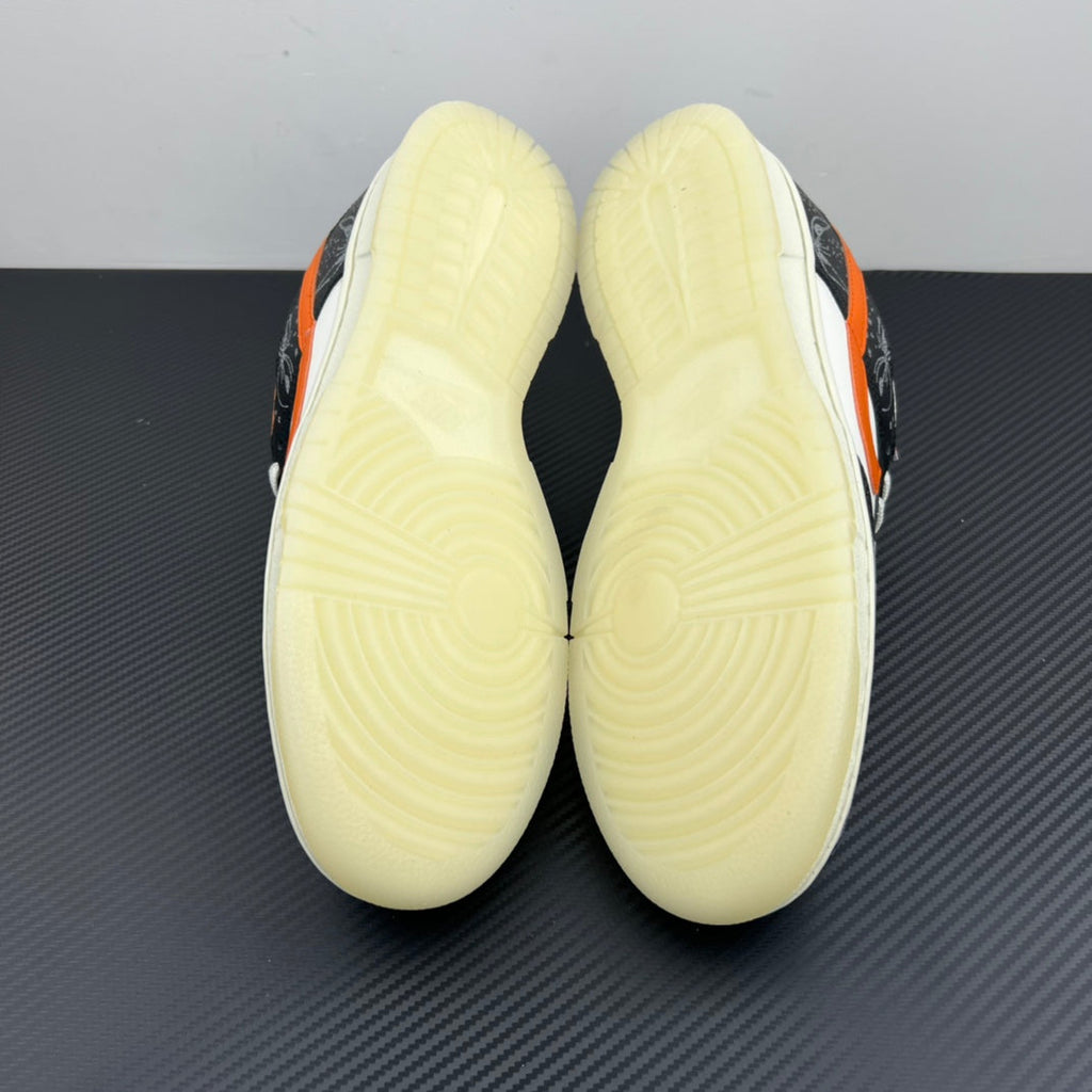 Low-top sneakers bottom view with pale yellow outsole treads; black and orange upper.