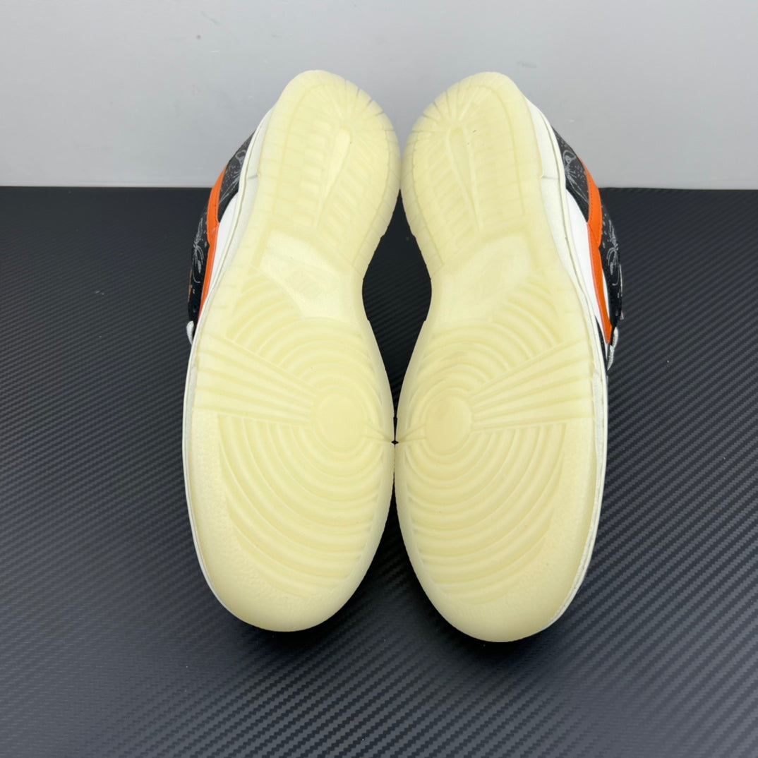 Low-top sneakers bottom view with pale yellow outsole treads; black and orange upper.
