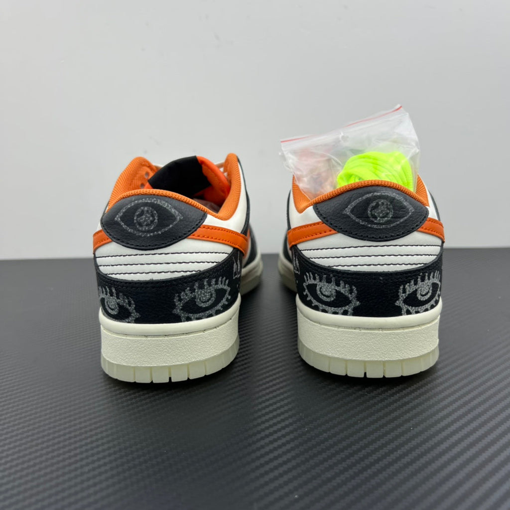 Low-top sneakers heel view: black rear panels, orange lining, white sole, side logo patch.
