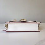 Coah bag side view, white body with burgundy trim and gold top clasp