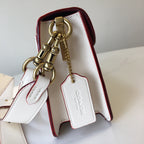 Coah bag, open with burgundy lining, gold charm and chain, white exterior