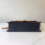 Navy handbag side profile with red-brown trim and gold clasp on top edge